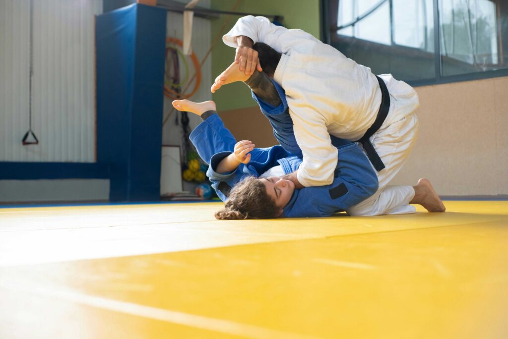 Two martial arts students practicing a throwing technique on training mats during a class.