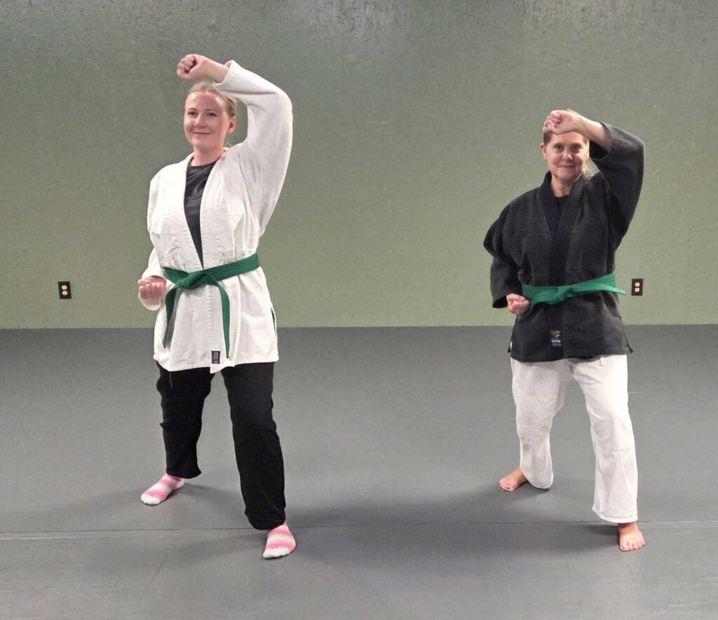 Two women practicing a martial arts pose during class.
